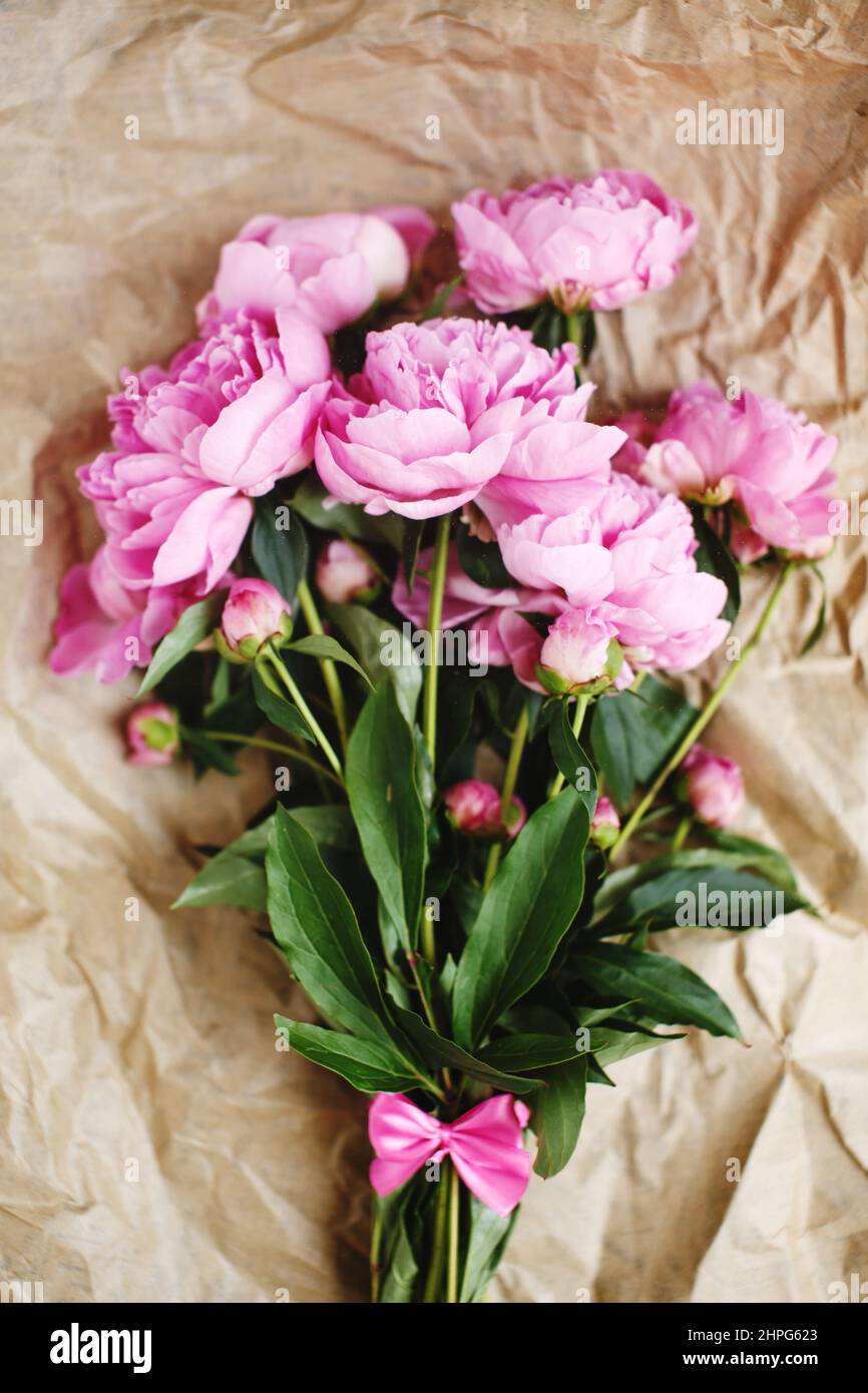 Tender bouquet of pink peonies flowers in sunlight on wrinkled craft paper background, top view, Valentine`s day Stock Photo